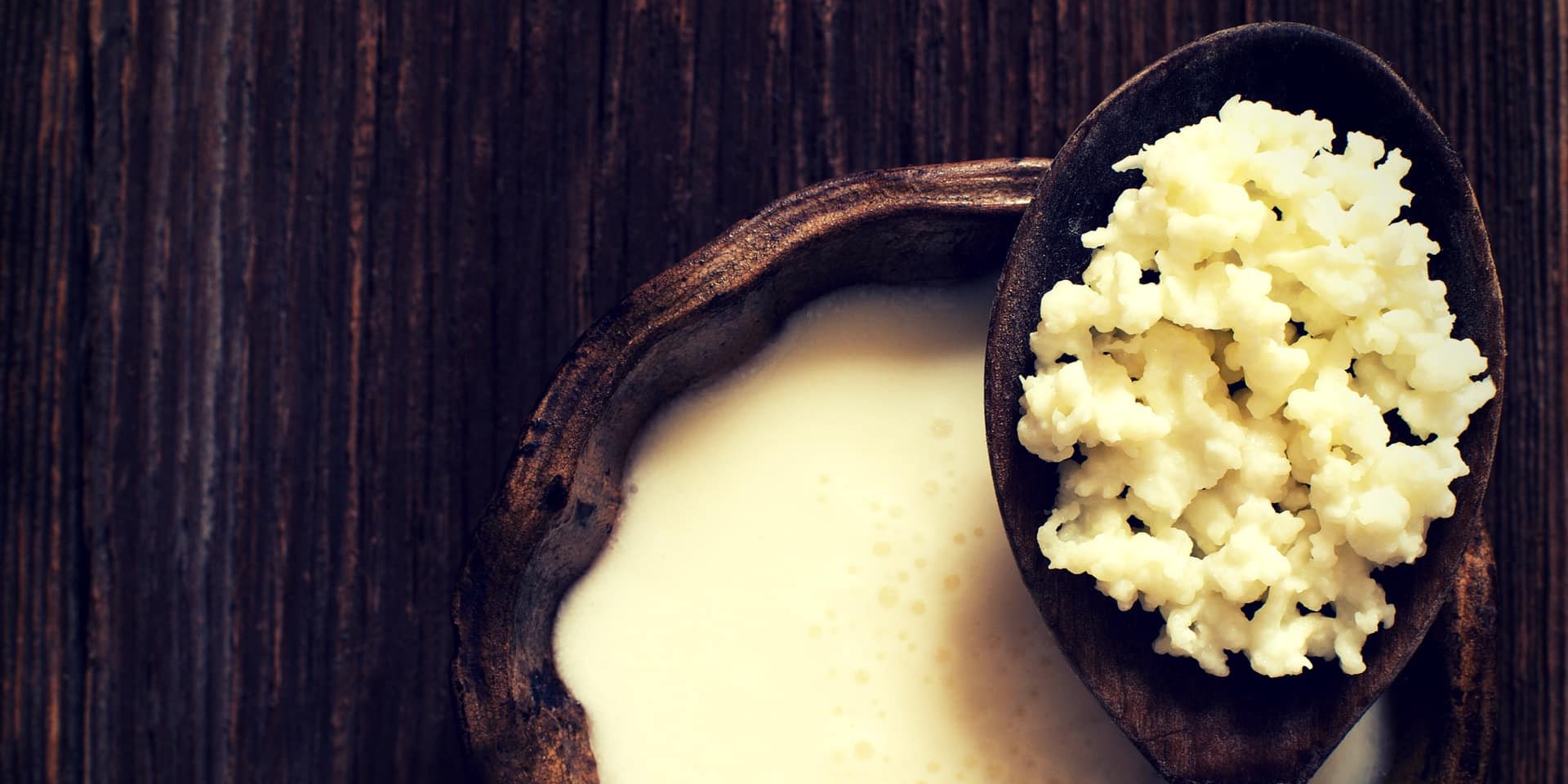 A wooden bowl of the best probiotic for constipation, kefir, with a spoonful of kefir grains on a wooden surface.