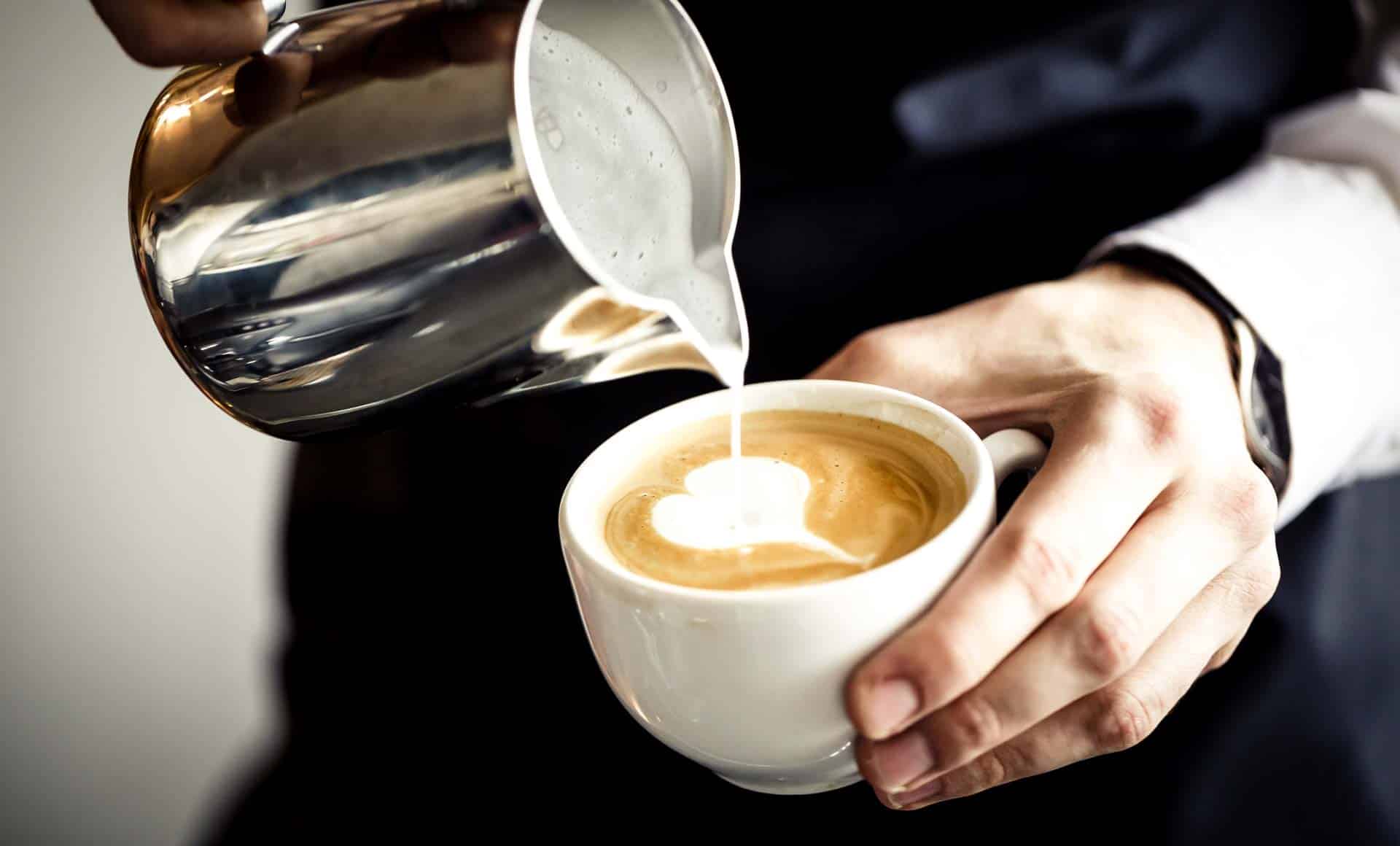 Barista pouring low carb steamed milk into a coffee cup to create latte art.