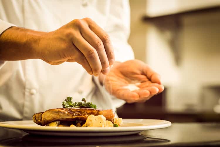 Closeup mid section of a chef putting salt in the kitchen
