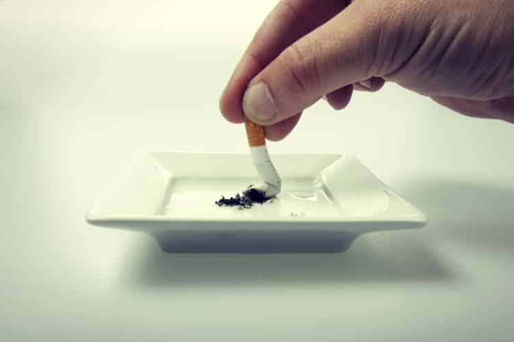 Hand stubbing out a cigarette on white ashtray