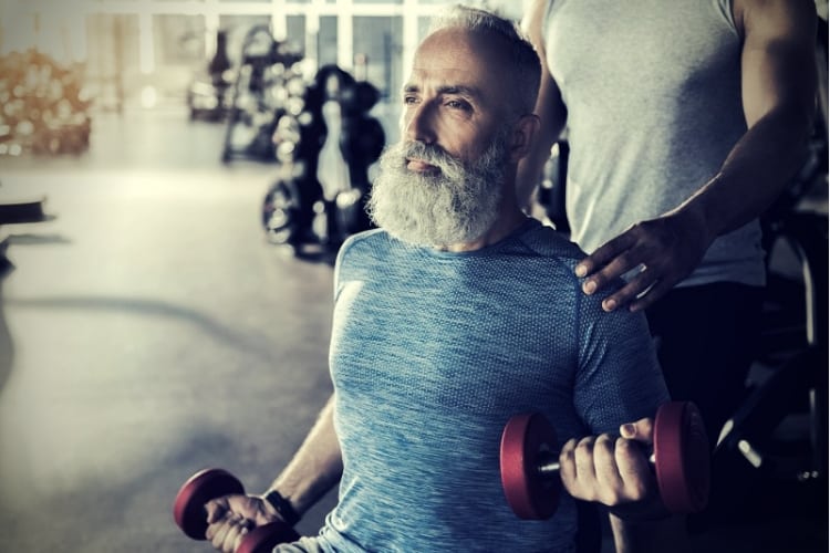 Serious bearded pensioner is doing exercises in athletic center