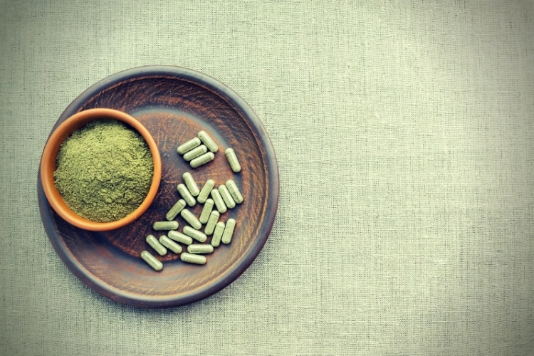 Supplement kratom green capsules and powder on brown plate Supplement kratom green capsules and powder on brown plate