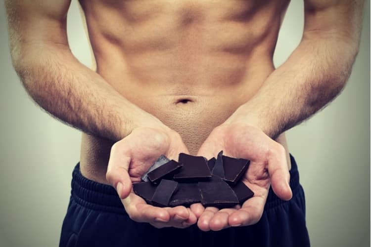 young fit man holding dark chocolate pieces
